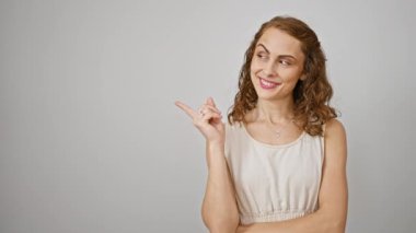 Neşeli genç bir kadın kulağından kulağa sırıtıyor ve kenarı işaret ediyor, izole edilmiş beyaz bir arka plana karşı duruyor. Güven telkin eden jestler, güven sunarken kameraya çekilen.