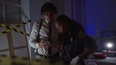 Bir kadın ve erkek polis ikilisi kapalı bir suç mahallinde akıllı telefondaki kanıtları analiz ediyor..