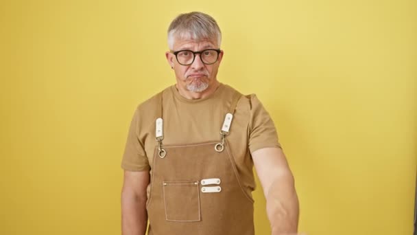 회색머리남자 안경이 앞치마가 씌여진 노란색 배경에 있습니다 어두운 표정으로 손가락을 — 비디오