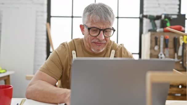 Handsome Senior Man Glasses Smiles While Using Laptop Carpentry Workshop — Stock Video
