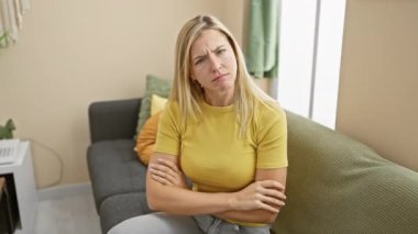 Şüpheci genç sarışın kadın, kollarını kavuşturmuş ve evde kaşlarını çatmış. Hoşnutsuzluğu dışa vurmak, olumsuz ifade güzelliğinin portresi kapalı alanlarda güvensizliğe gömülü. 