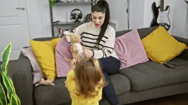 Bir kadın ve genç bir kız modern bir oturma odasındaki rahat bir kanepede oyuncak ile oynuyorlar.