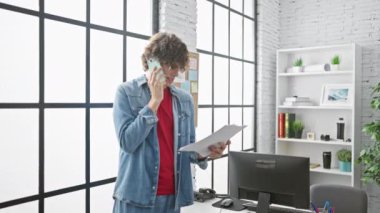 Kot giyen genç adam modern ofiste belgelerle telefonda konuşuyor.