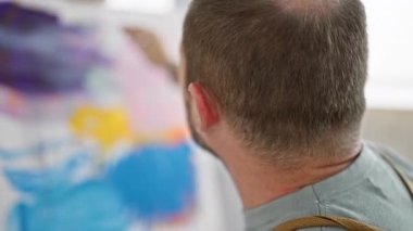 Olgun bir adam, sanatsal ifade ve hobi sergileyerek arka planda yakalanan, kapalı bir stüdyo ortamında yaratıcı bir şekilde resim yapıyor..