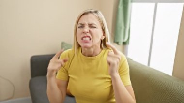 Tişört giyen sinirli genç sarışın kadın kulaklarını parmaklarıyla kapatıyor, evdeki yüksek sesli müzik sesiyle strese giriyor sağır yüz ifadesi. 