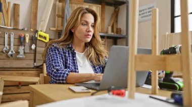 Şok olmuş ve korkmuş, genç ve güzel Latin kadın marangozluk masasında oturuyor, atölyenin ortasında yüzüne kazınmış afallamış bir ifadeyle.