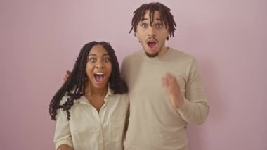 Neşeli galibiyet! Güzel bir çift, muzaffer, pembe izole edilmiş arka planda duruyorlar, eller yukarıda, zafer çığlıkları atıyorlar. Onların kendine güveni, neşeli ifadeleri mutluluk ve başarının çığlığı..