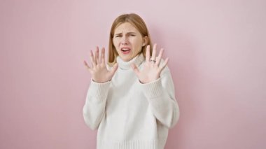 Korkmuş sarışın kız panik içinde bağırıyor, ifadesindeki korku, duruş hareketi olarak ellerini kaldırıyor - pembe arka planda izole edilmiş güzel kız.