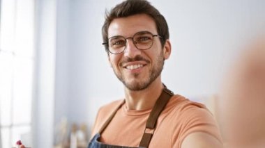 Gözlüklü ve sakallı, parlak kapalı bir ortamda gülümseyen genç İspanyol adam, gündelik ve yaklaşılabilir bir tavır sergiliyor..