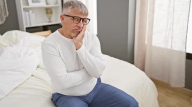 Sıkılmış, yorgun, orta yaşlı, pijamalı, gri saçlı, depresyon problemleri hakkında derin düşünen, kollarını yatak odasının hücre hapsinde birleştiren bir adam..
