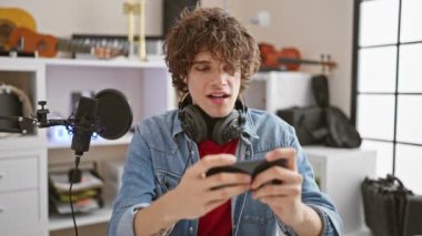 Kıvırcık saçlı genç bir İspanyol, müzik stüdyosunda akıllı telefonuyla çeşitli duygular ifade ediyor..