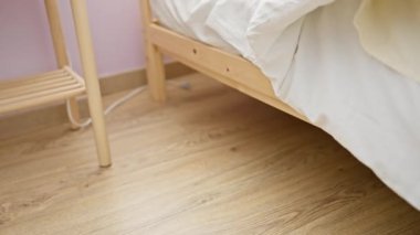 Açık pembe duvarları ve minimalist mobilyaları olan bir yatak odasında, tahta bir yatakta çıplak ayakla sallanan bir kadının çıplak ayak görüntüsü..