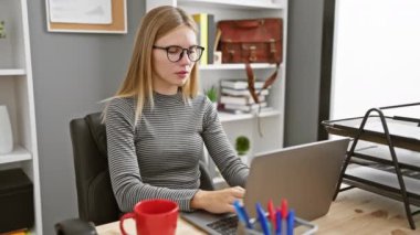Modern ofiste dizüstü bilgisayarla çalışan odaklanmış bir kadın masasındayken farklı duygular ifade ediyor..