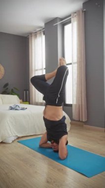 Modern bir yatak odası ortamında yoga başlığı üzerinde asanas antrenmanı yapan atletik kıyafetli bir adam denge ve zindelik gösterisi yapıyor..