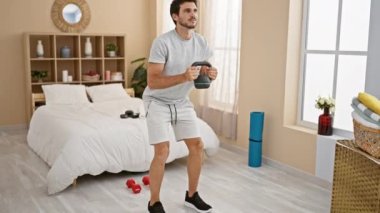 Güzel bir yatak odasında kettlebell ile egzersiz yapan yakışıklı bir adam.