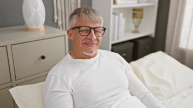 Beyaz saçlı, gururla yatak odasında kendini gösteren neşeli orta yaşlı bir adam. Pijamalarına güvenen, bulaşıcı ve mutlu bir ifade sergileyen....