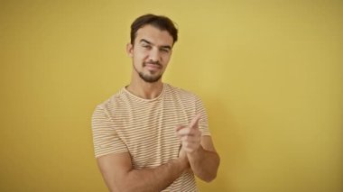 Çizgili tişört giyen genç İspanyol adam gülümsüyor mutlu bir şekilde elini ve parmağını yalıtılmış sarı arka planda gösteriyor.