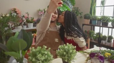 Bir adam ve bir kadın çiçekçi çiçekçi çiçeklerle dolu bir çiçekçide selfie çekiyorlar..