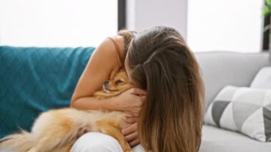 Kendine güveni tam, İspanyol bir kadın evdeki kanepede köpeğiyle samimi bir öpücükten zevk alıyor, neşeli bir gülümseme sergiliyor.