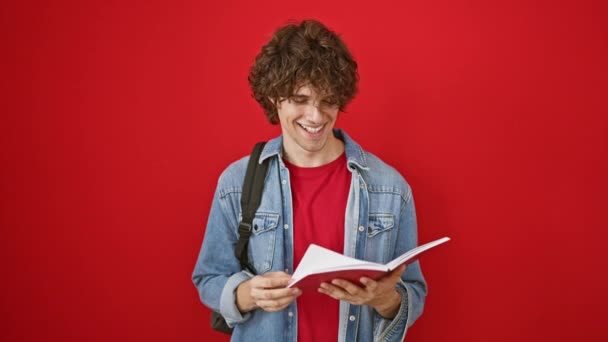 鮮やかな赤い背景に本を読んでいるカーリーヘアと微笑む若い男 — ストック動画