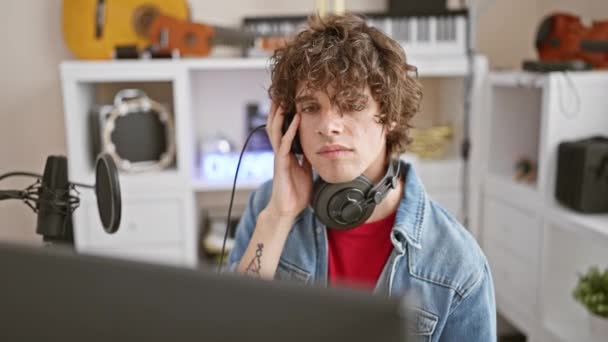 头发卷曲的男人穿着耳机和牛仔夹克 聚精会神地在音乐工作室里 — 图库视频影像