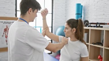 Terapist adam, güneşli fizyoterapi kliniğinde hasta kadına yardım ediyor ve kol rehabilitasyonu uyguluyor..