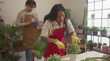 Erkek iş arkadaşı önlüklü tablet kullanırken, çiçekçi kadın içeride çiçek düzenliyor..