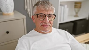 Neşeli orta yaşlı, kır saçlı, evde poz veren, yüzünde parmakları olan barış işareti olan, rahat bir evde pijama giyen, mutlu bir zafer ışıldayan bir adam..