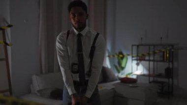 Odaklanmış bir Afro-Amerikan dedektifi ev içi bir suç mahallinde silahını doğrultuyor..