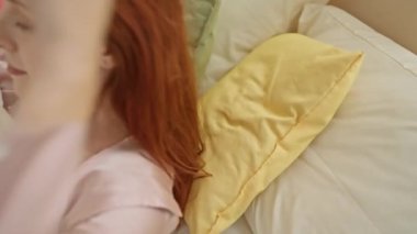 Kızıl saçlı kadın huzurlu bir şekilde dinleniyor, rahat bir yatak odasında, gözleri sakin bir ifadeyle kapalı..