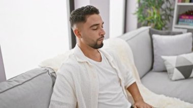 Sükunetin tadını çıkar, genç, yakışıklı bir Arap adam oturma odasındaki kanepesinde zen 'i canlandırıyor, yoga meditasyonu ile barışı teşvik ediyor ve gözleri kapalı rahatlama pozu veriyor.