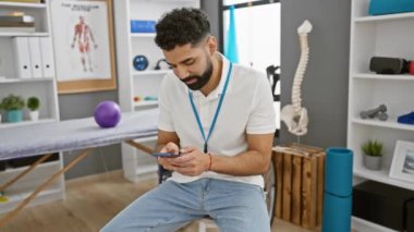 Parlak bir rehabilitasyon kliniğinde sakallı İspanyol terapist akıllı telefondan mesaj atıyor ve modern sağlık hizmetleri anlayışını aktarıyor..