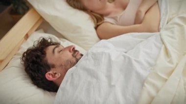 Üzgün bir kadın yatarken partneri yatak odasında huzur içinde uyuyor. İlişki dinamiklerinin altını çiziyor..