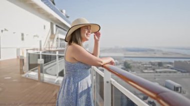 Şapkalı gülümseyen bir kadın, deniz manzaralı bir yolcu gemisinin güvertesinde güneşli bir günün tadını çıkarır..