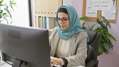 Orta yaşlı İspanyol kadın tesettürlü, modern ofis içi bilgisayar bölümünde çalışıyor..