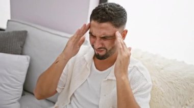 Stresli, sakallı, evinde koltukta oturan genç bir Arap adam, yakışıklı yüzünde depresif bir ifade, başı üstünde, şiddetli migren ağrısı çekiyor - iç mekanda üzücü bir sahne.