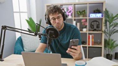 İspanyol bir adam modern bir stüdyoda mikrofon, dizüstü bilgisayar ve canlı yayın ile bir podcast sunuyor.