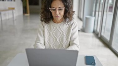 Modern ofis içinde dizüstü bilgisayarda çalışan gülümseyen İspanyol kadın..