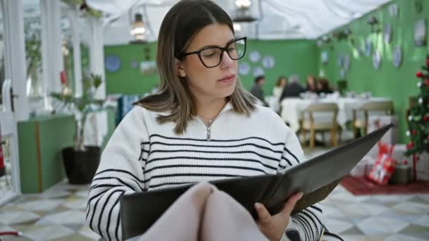 Dospělá Žena Brýlích Zkoumající Menu Zamyšleně Moderní Restauraci Vánoční Výzdobou — Stock video