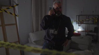 Ciddi bir orta yaşlı dedektif. Sakallı bir dedektif. Kapalı bir suç mahallinde telefon görüşmesi yapıyor.