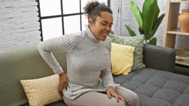 Kanepede sırt ağrısı çeken kıvırcık saçlı Afrikalı Amerikalı kadın.