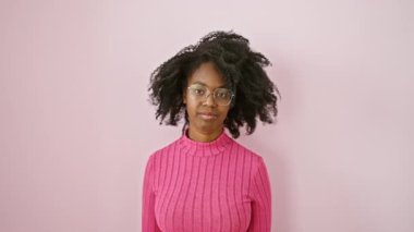 Gözlüklü afro-amerikan kadın şaşırıyor, işaret ediyor ve eğleniyor, pembe bir odada duruyor.