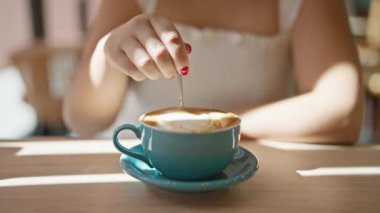 Güneşli kafe sahnesi, bardaklı güzel İspanyol kadın kahve molası veriyor, masada oturuyor ve sıcak kafeteryada espresso içiyor.
