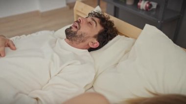 Bir çift yatak odasında rahatlıyor, bir erkek ve kadını rahat, kapalı bir odada yatakta birlikte yatarken gösteriyor..