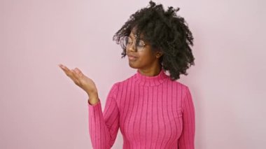 Gözlüklü neşeli Afro-Amerikalı kadın, sunuma hazır, içten gülümseyen ve misafirperver, bir iş ortamında el kol hareketi yapan