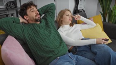 Bir erkek ve bir kadın, rahat bir oturma odasında, kanepede birlikte rahatlar, umursamadan televizyon izlerler..