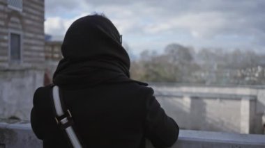 İstanbul 'daki tarihi Osmanlı mimarisine tepeden bakan kapüşonlu giysili düşünceli bir kadının arka görünüşü..