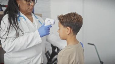 Beyaz önlüklü bir kadın doktor, tıp bürosunda genç bir erkek hastaya termometre kullanıyor..