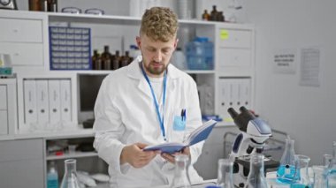 Laboratuvar ortamında kitap okuyan sakallı beyaz bir adam. Etrafı bilimsel ekipman ve cam parçalarıyla çevrili.