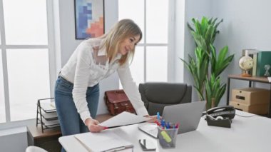 Ofiste duran bir iş kadını bilgisayarın ve telefonun yakınındaki belgeleri karıştırıyor..